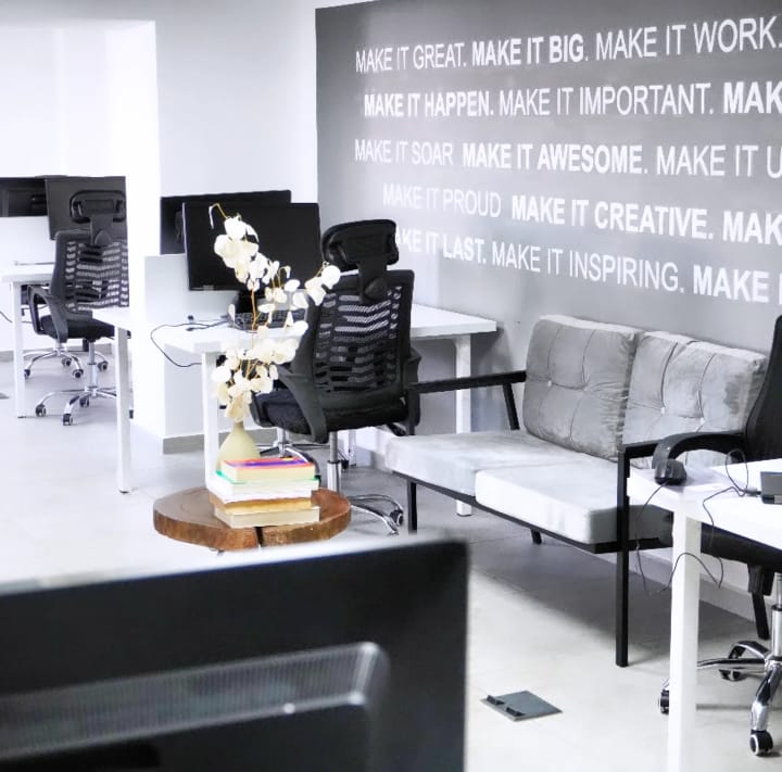 A modern office space with white desks, black ergonomic chairs, and a large motivational quote mural on a gray wall.
