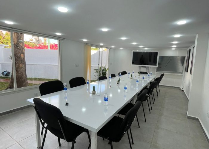 A modern, well-lit meeting room at Al Hub Coworking Space in Rabat, featuring a long white conference table set with chairs and water bottles, ready for a meeting or presentation.